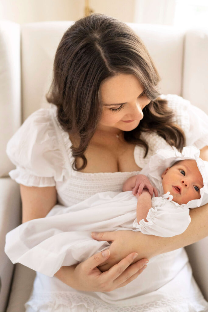 Mother holds baby in white outfit in her arms. 