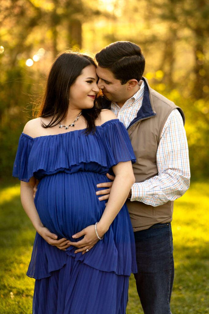 Pregnant woman in blue dress being hugged from behind by husband.