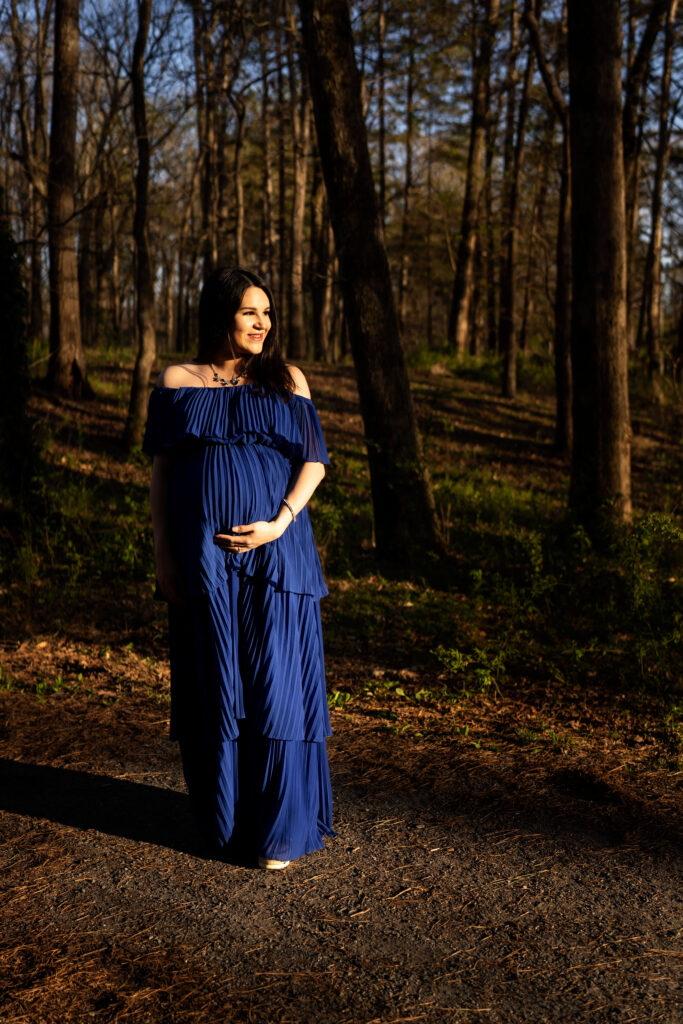 Pregnant woman in forest smiling to the right of scene.