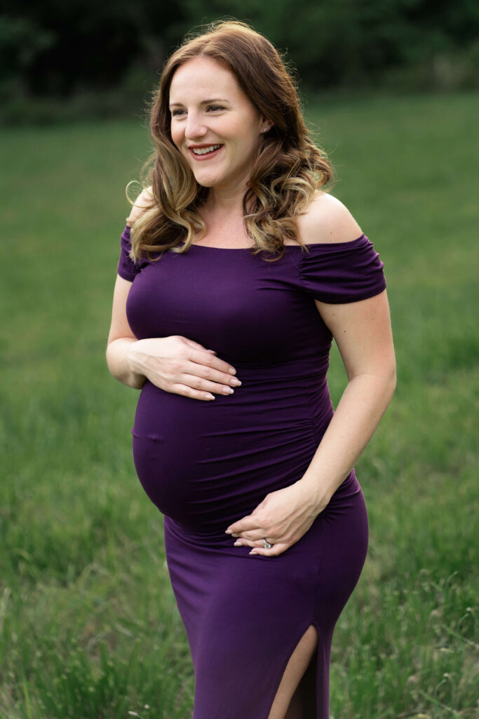 Pregnant woman in purple dress smiling to camera left. 