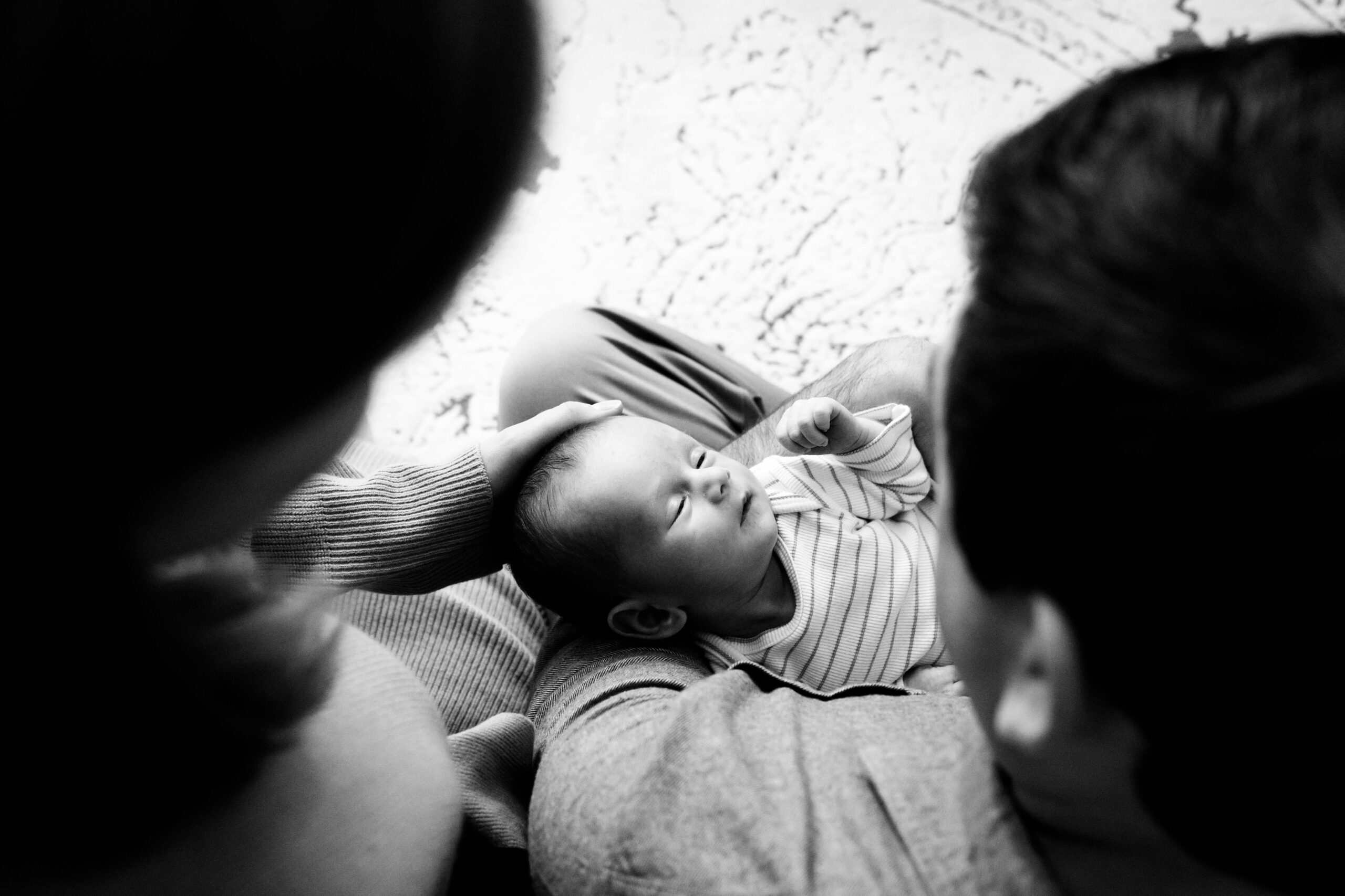 Black and white image shot from above of newborn baby in parents' arms
