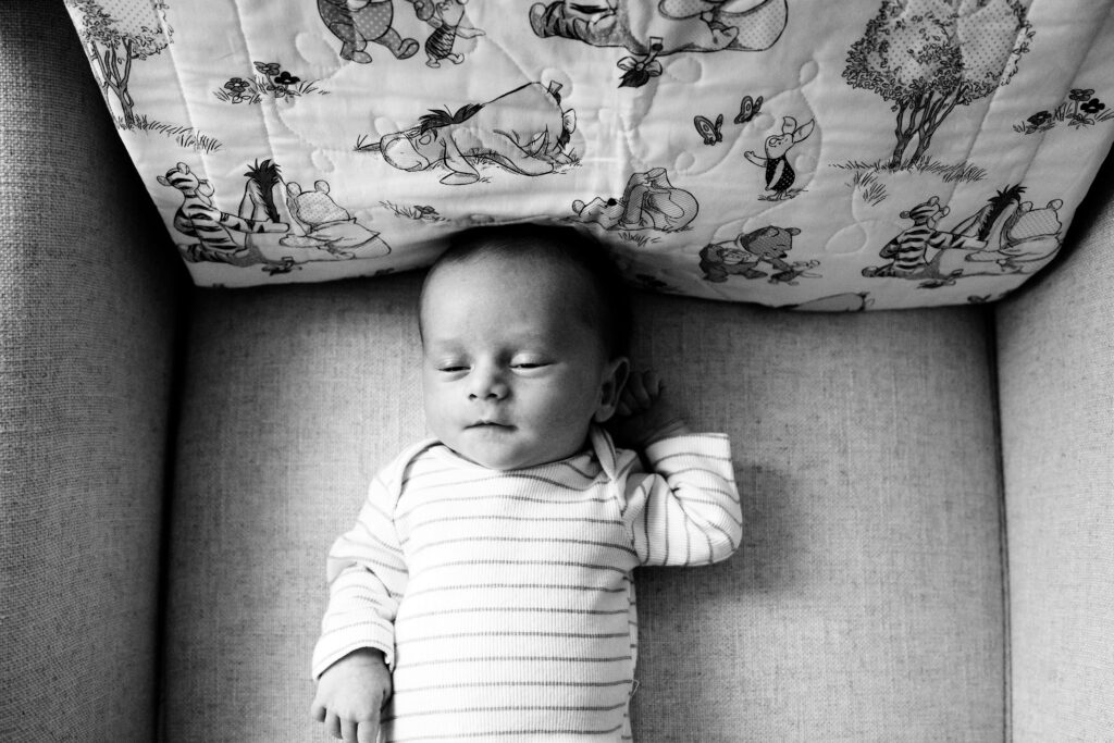 black and white image of newborn baby laying on chair with winnie the pooh blanket