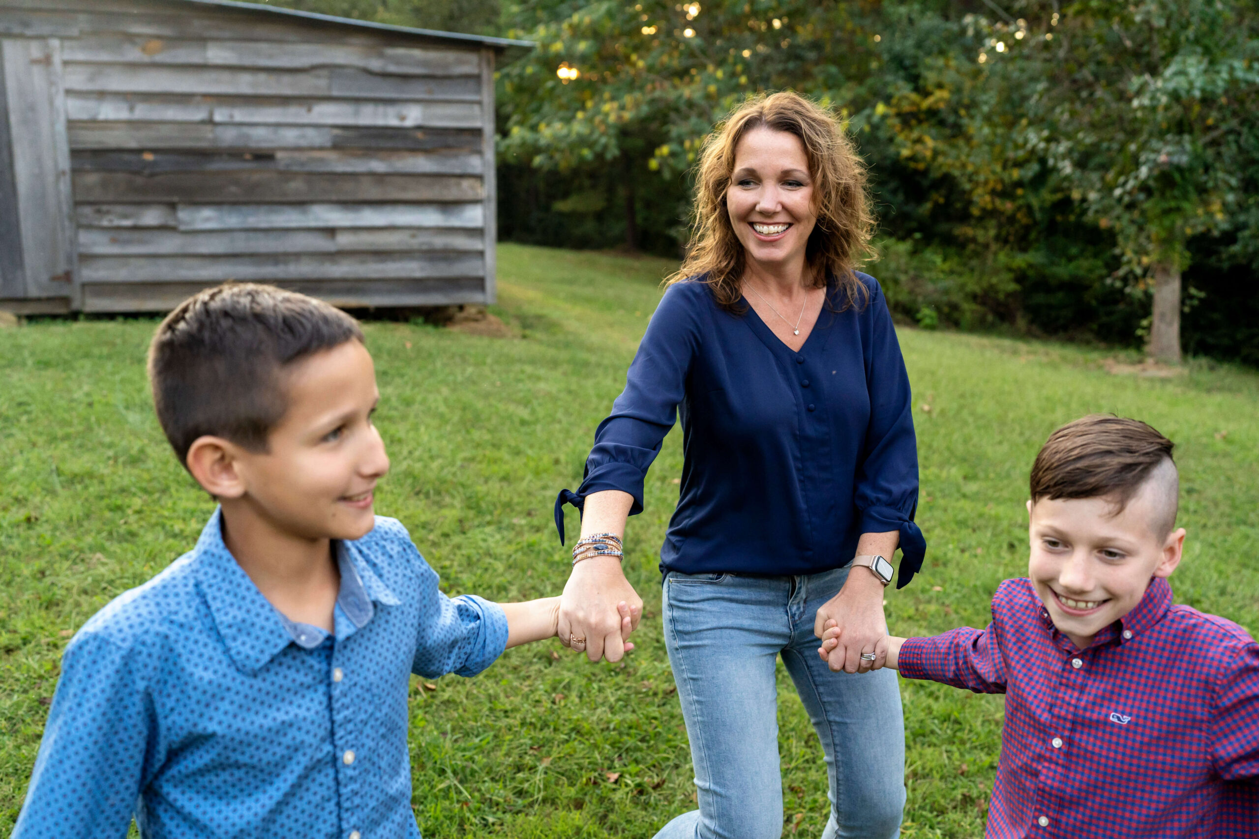 Mother smiling at two sons while holding their hands in a grassy field.